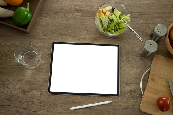 Dijital tablet ve bir kase sağlıklı vejetaryen salatası ev mutfağındaki ahşap masada..