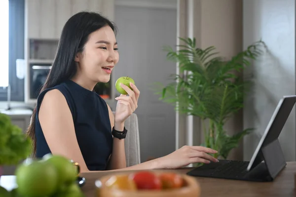 Χαρούμενη Νεαρή Γυναίκα Τρώει Μήλο Και Χρησιμοποιώντας Tablet Υπολογιστή Στην — Φωτογραφία Αρχείου