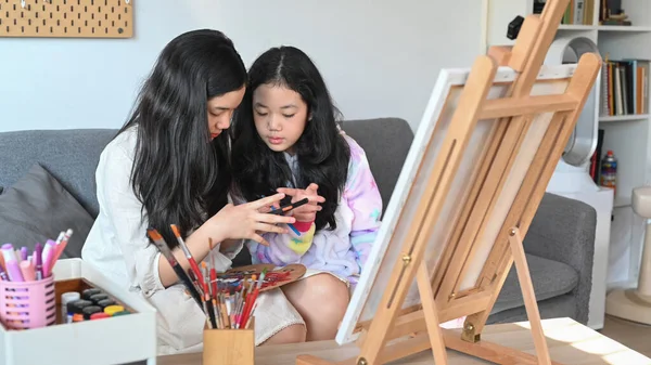 Two cute asian girls painting picture in living room while spending leisure time together.