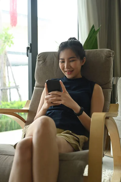 여자가 안락의자에 앉아서 스마트폰으로 메시지나 미디어를 확인하는 — 스톡 사진