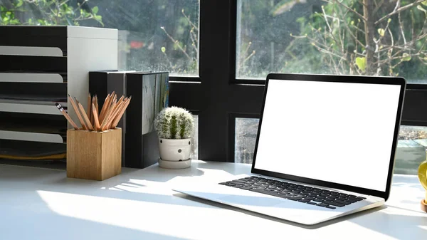 Laptop computer and supplies on white table. Blank screen for text message or information content.