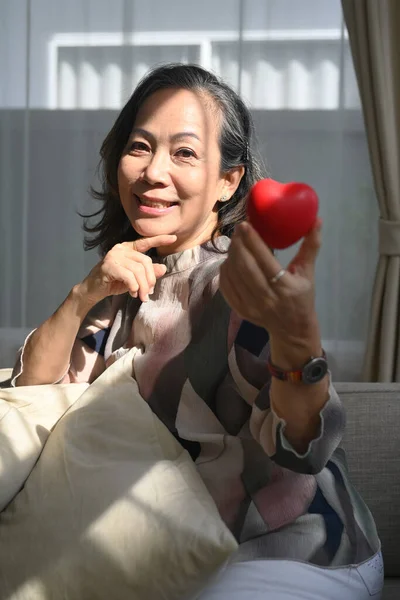 中年妇女手握心形 对着相机微笑 老年人护理 心脏健康和老年人生活质量概念 — 图库照片