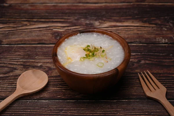 Nutritious rice porridge with soft boiled egg and spring onion in wooden bowl for breakfast or light meal.