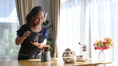 Mutfak masasında durmuş, kahve demliyor ve sabahları eğleniyor..