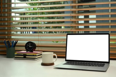 Laptop bilgisayarı, kahve fincanı ve beyaz masadaki malzemelerle rahat bir ofis..