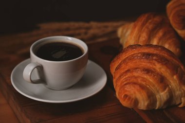 Bir fincan kahve ve taze pişmiş kruvasan ahşap masa. Havalandırma, ekmek fırını ürünleri kafe konsepti.