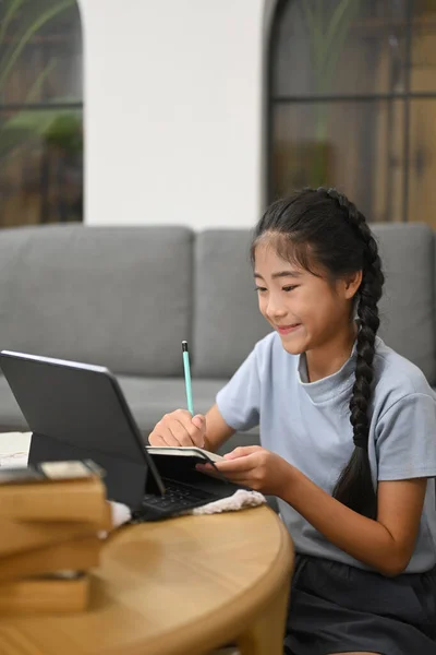 Smiling preteen girl having learning online at virtual class on laptop computer while sitting in living room. Concept of Virtual education, homeschooling.