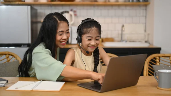通过在线学习系统帮助女儿做作业的亚洲妈妈笑着 — 图库照片
