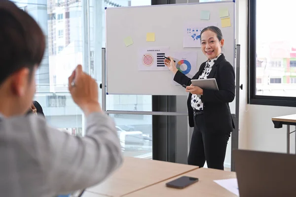 Confident business woman team leader standing near flip chart with graphs diagrams, presenting market research results at meeting.
