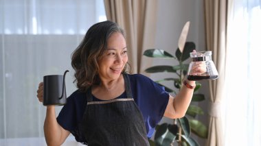 Elinde siyah çelik çaydanlıkla mutlu bir orta yaşlı, sabah kahvesinin tadını çıkarıyor..