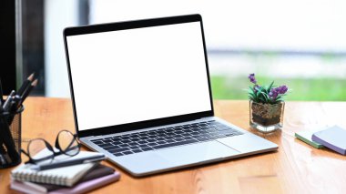 Diz üstü bilgisayar, gözlük, not defteri ve kalem tutacağı ahşap ofis masasında..