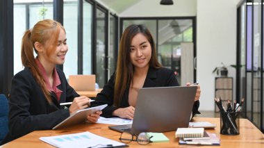 Asyalı iş kadını, iş arkadaşıyla bilgisayar laptopunda proje planlarını tartışıyor..