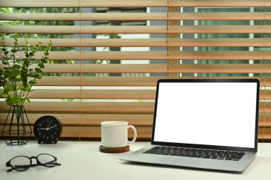 Boş ekranlı bilgisayar bilgisayarı, kahve fincanı, bardaklar ve ev bitkisi beyaz masada..