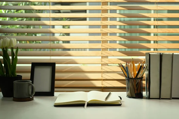 Comfortable workplace with books, picture frame, coffee cup, pencil holder and flower pot on white table. Home office desk.