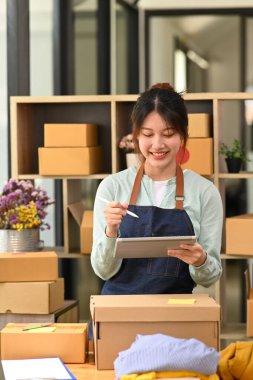 Gülümseyen kadın çevrimiçi satıcı dijital tabletten ürün satın alma siparişini kontrol ediyor. E-ticaret, çevrimiçi iş, çevrimiçi satış kavramı.