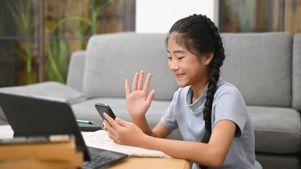 Smiling asian girl sitting on floor in living room and using mobile phone during learning online. Concept of Virtual education, homeschooling.