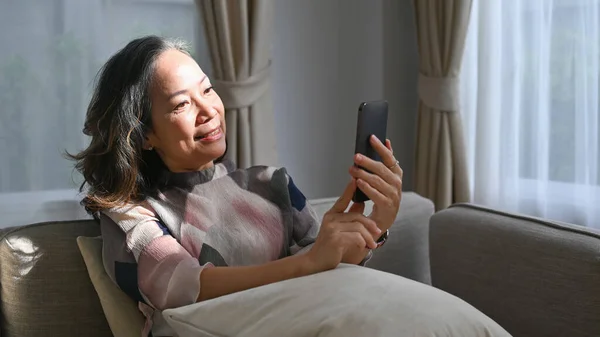 Evdeki Koltukta Akıllı Telefon Kullanarak Gülümseyen Emekli Kadın Emeklilik Teknoloji — Stok fotoğraf