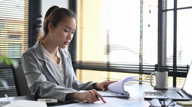 Şirket işlemlerini yürüten Asyalı yönetici, ticari verileri analiz eden, ofis masasında pazarlama planları yapan.