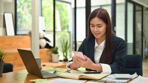 Asian woman employee sitting at office desk and using smart phone.
