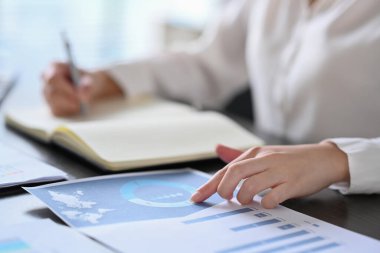 Finansal istatistik grafiğini analiz eden ve not defterine bilgi yazan profesyonel iş kadınını kapat.