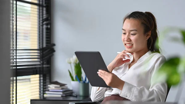 Pleasant asian female office worker reading information on digital tablet.