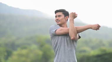 Spor kıyafetli genç bir Asyalı kollarını esnetiyor, sabah antrenmanından önce dışarıda ısınıyor. Sağlıklı yaşam tarzı, egzersiz ve sağlık konsepti.