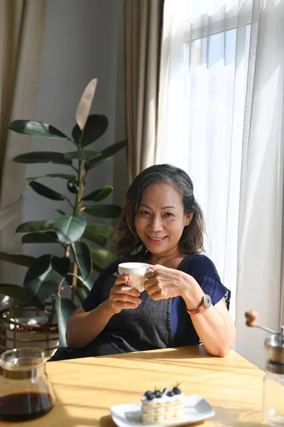 Oudere Vrouw Met Koffiebeker Terwijl Naast Het Raam Thuis Zit — Stockfoto