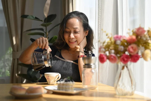 满意的中年妇女在明亮的客厅里坐在窗边 一边喝着黑咖啡 一边开始新的一天 享受生活的概念 — 图库照片