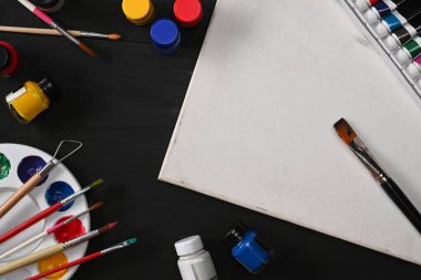 Boya fırçalı boş tuval, tüp boyası, suluboya ve palet boş ahşap masada. Yaratıcılık, DIY konsepti.