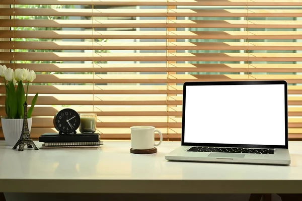 Laptop computer with white screen display, coffee cup, books and flower pot on white table.