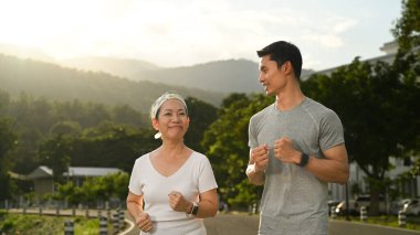 Parkta kişisel antrenörüyle koşan orta yaşlı mutlu bir kadın. Sağlıklı yaşam tarzı ve uygunluk kavramı.