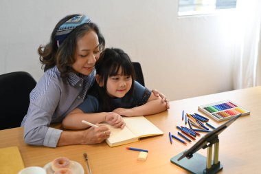 Sevecen orta yaşlı bir büyükanne, tatlı bir torunla resim çiziyor. Oturma odasında birlikte hafta sonu aktivitelerinin keyfini çıkarıyor..