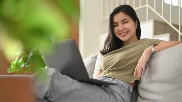 여자에게 소파에서 노트북을 사용하여 평상복을 입히고 집에서 시간을 보내는 — 스톡 사진