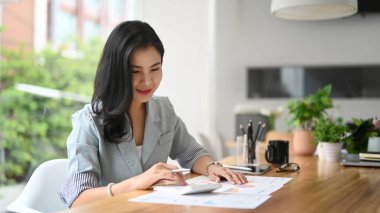 Finansal raporları kontrol eden ve verileri hesaplamak ve özetlemek için hesap makinesi kullanan genç bir girişimci..