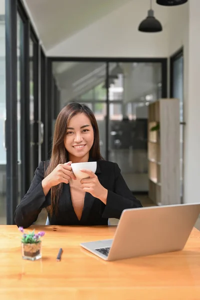 Confident asian woman entrepreneur holding coffee cup and smiling at camera.