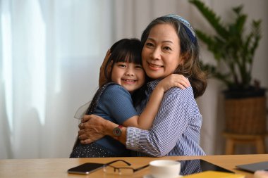 Şefkatli bir büyükanne tatlı torununa sarılıyor ve kameraya gülümsüyor. Aile ilişkileri kavramını sevmek.