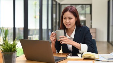 Çekici genç girişimci elinde kahve fincanı ile dizüstü bilgisayarında internetten webinar izliyor..