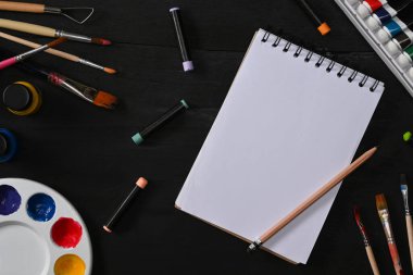 Çizim kitabı, fırçalar, tüp boyası, suluboya ve palet siyah ahşap masada. Sanatçı atölyesi, Sanat, atölye, resim, yaratıcılık kavramı.