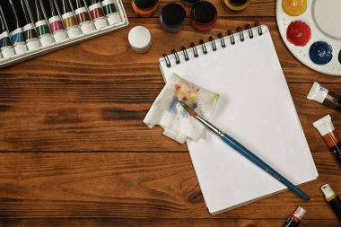 Üst görünüm eskiz defteri, boya fırçaları, tüp boya, suluboya ve ahşap arka planda palet. Sanat, atölye, resim, yaratıcılık kavramı.