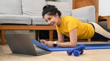 Spor yapan bir kadın apartmandaki spor salonunda spor yaparken dizüstü bilgisayarda ders seyrediyor..