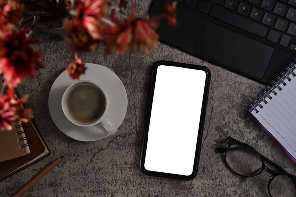 Smart phone with white display, coffee cup, eyeglasses and notebook on stone background.