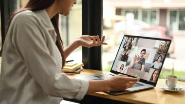 Kırpılmış çekim genç iş kadını modern iş yerinde otururken online video görüşmesi yapıyor..