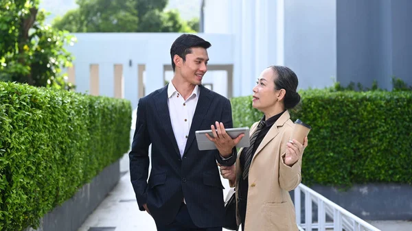 Businesspeople having discussion business plan on digital tablet and walking outside modern office building.