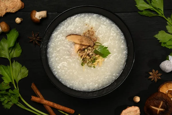 Rice porridge or congee with shiitake mushroom, boiled egg ,sliced ginger and slice scallion in bowl on black wooden table.