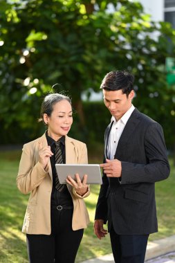 Başarılı yatırımcılar ofis binasının önünde duruyorlar ve dijital tablette yeni proje gelişimini tartışıyorlar..