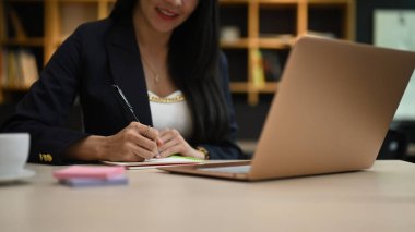Dizüstü bilgisayar kullanan ve not defterine iş planı yazan kadın girişimci görüşü.