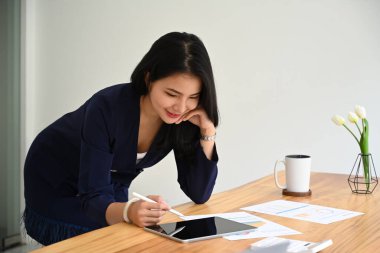 Finansal raporlarla çalışan ve ofis masasında dijital tablet kullanan çekici bir kadın muhasebeci..