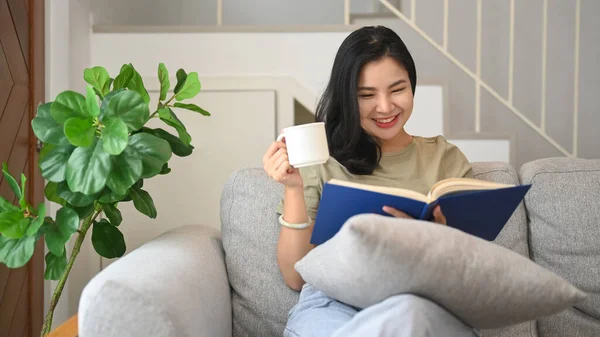 松懈的年轻女子在家里看书 在舒适的沙发上喝咖啡 — 图库照片