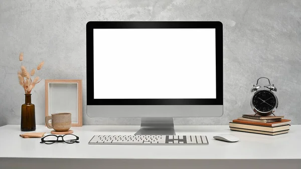 Front view computer with empty display, picture frame, books and alarm clock on white table.