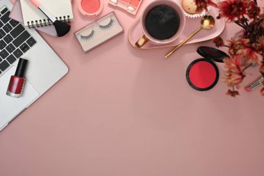 Feminine workspace with laptop, makeup brushes and cosmetics on pink background. Top view with copy space.